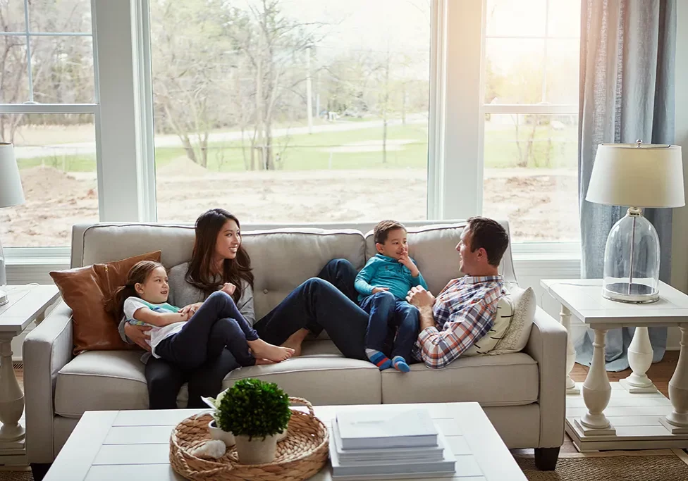 family-enjoying-living-room-natural-light-windows-doorsnmore-barry-il Happy family relaxing in a sunlit living room with large energy-efficient windows - Contact Doors N More in Barry, IL today!